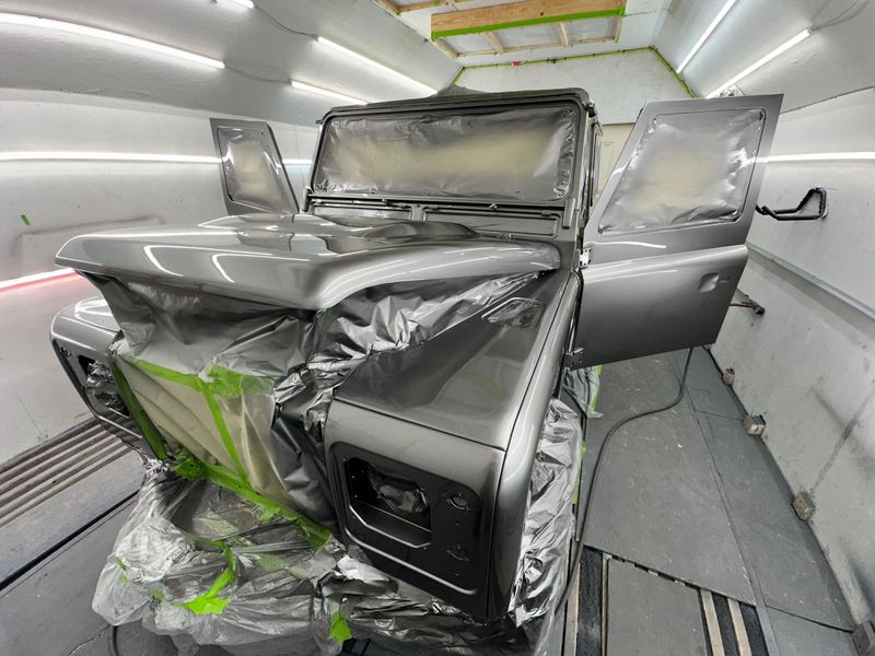 Land Rover Defender in the paint booth with doors open, freshly coated in satin dark grey, windows and interior still masked